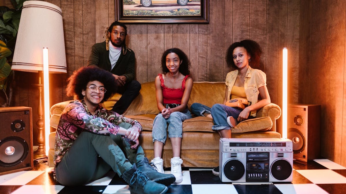 A diverse group of young adults sitting in a vibrant, retro-themed room with a boombox and vintage decor.